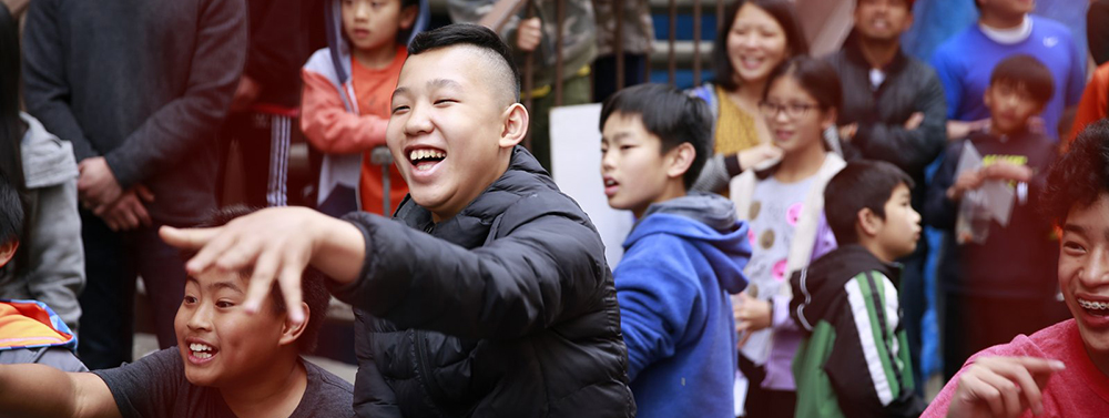 a boy throws a bean bag at Dunko at the 70th annual cameron carnival, he is surrounding by excited smiling faces